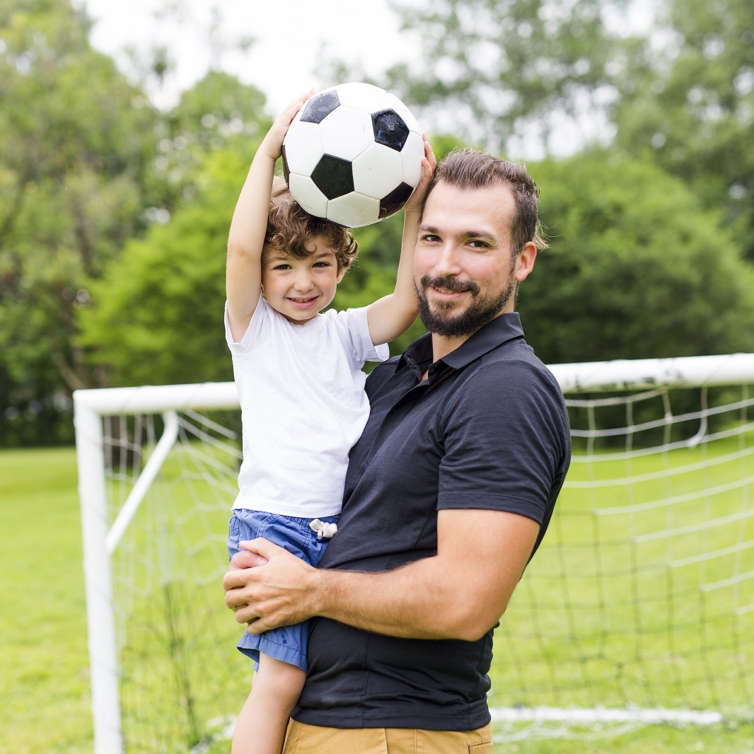 Homem com uma criança no colo em um campo de futebol